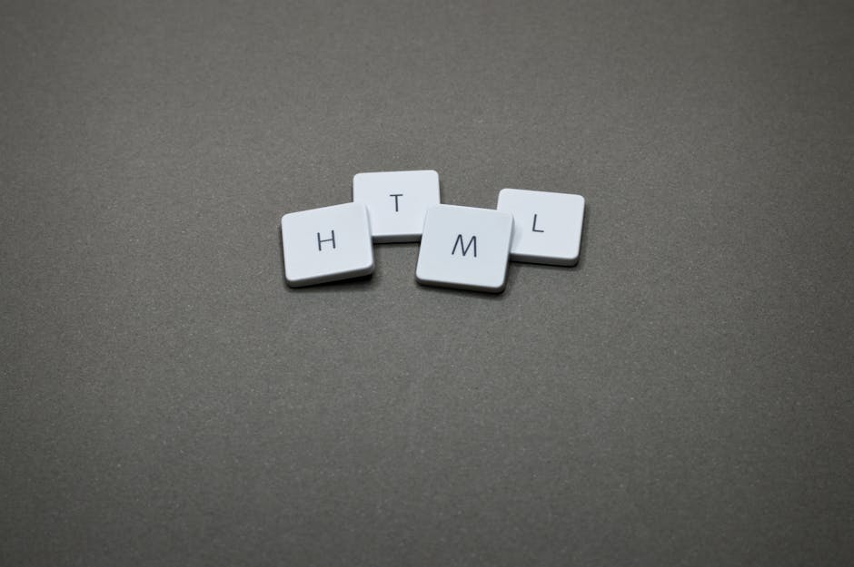 Close-up image of four white tiles with black letters spelling 'H T M L' arranged in a semi-circle on a smooth, dark gray surface. The tiles are made of glossy plastic and are evenly spaced, with the